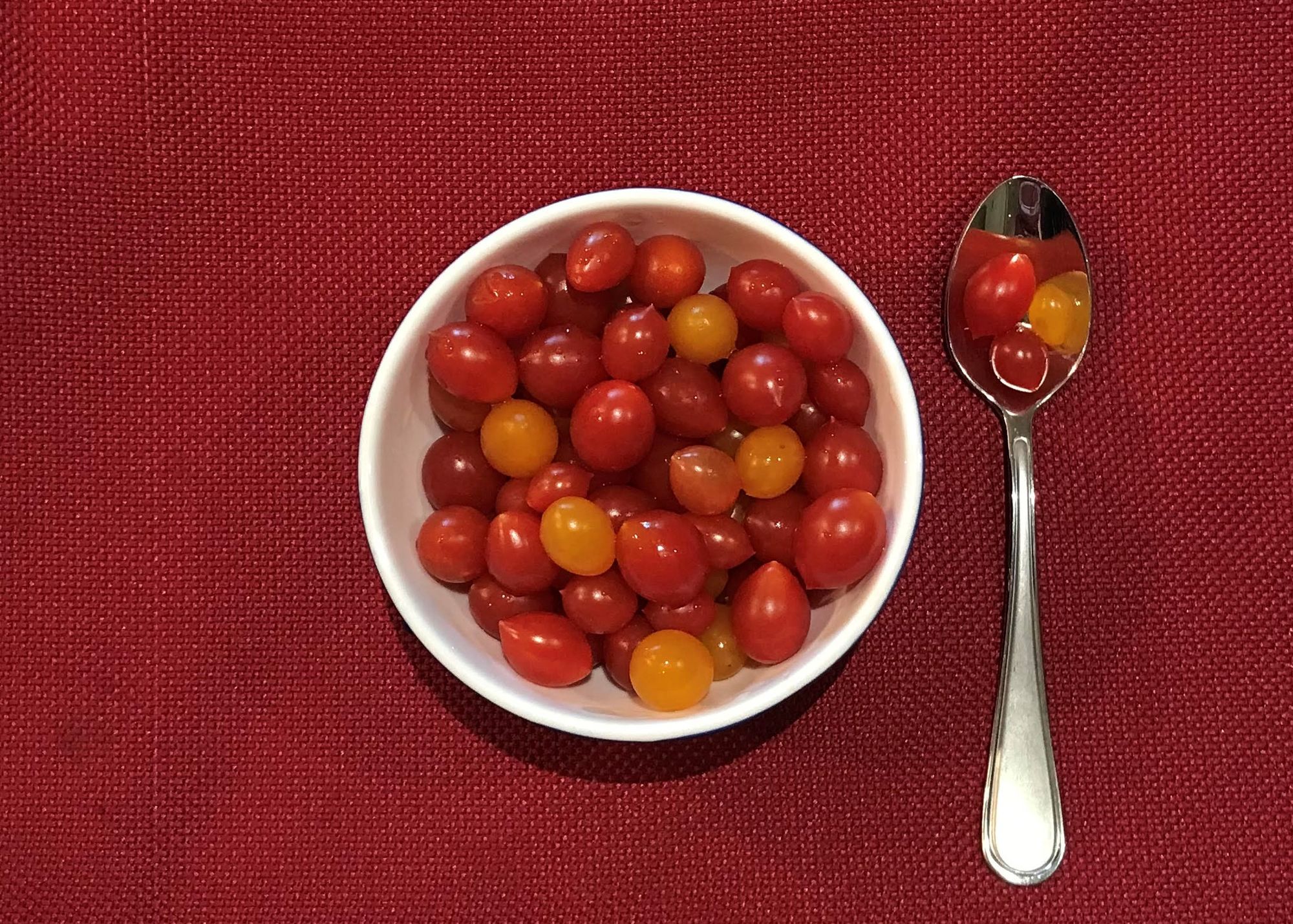 Small bowl of tiny red and yellow tomatoes. Teaspoon holding 3 tiny tomatoes.