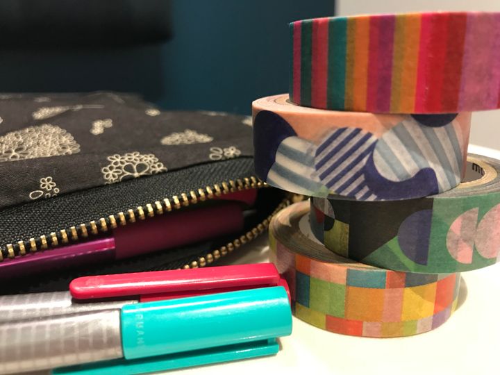 Stack of washi tape next to a pencil case and some pens.